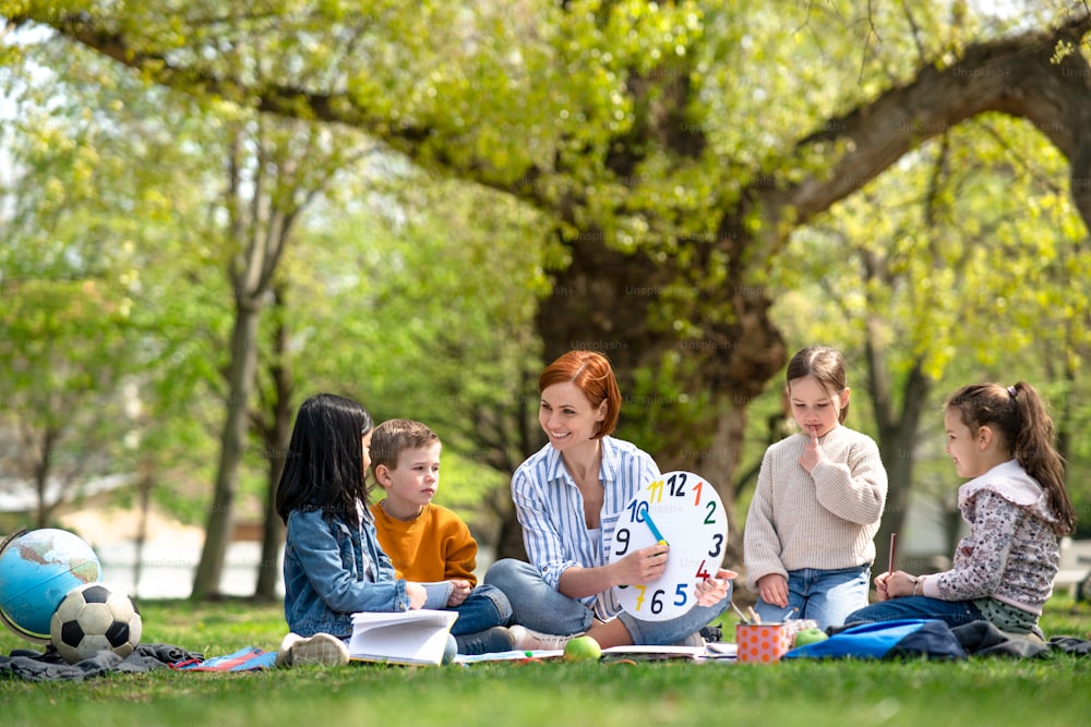 Ein Lehrer mit kleinen Kindern sitzt draußen im Stadtpark, Lerngruppen-Bildungskonzept.