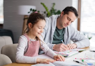 Père aidant la petite fille à faire ses devoirs à l’intérieur à la maison, à distance.