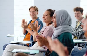 A portrait of cheerful university student sitting and studying in classroom indoors, clapping.