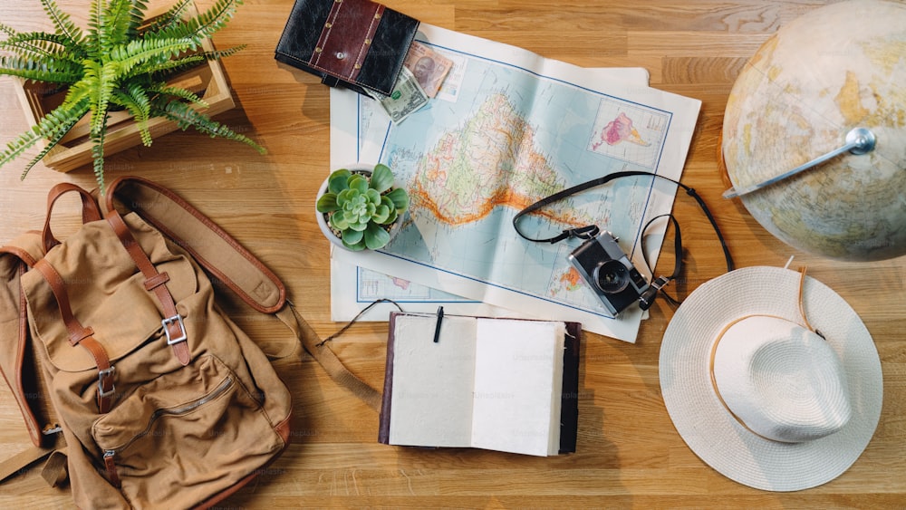 ラップトップ、地図、その他の旅行の必需品、木製の背景を備えたフラットレイトップビューデスクトップ旅行コンセプト。