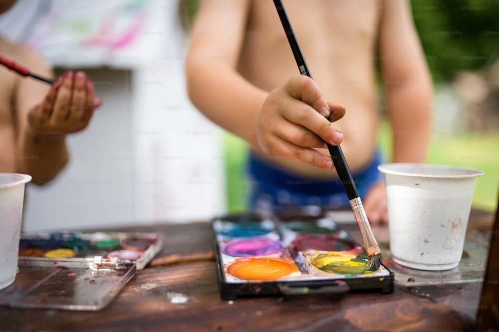 Midsection of unrecognizable boy and girl painting outdoors in summer.