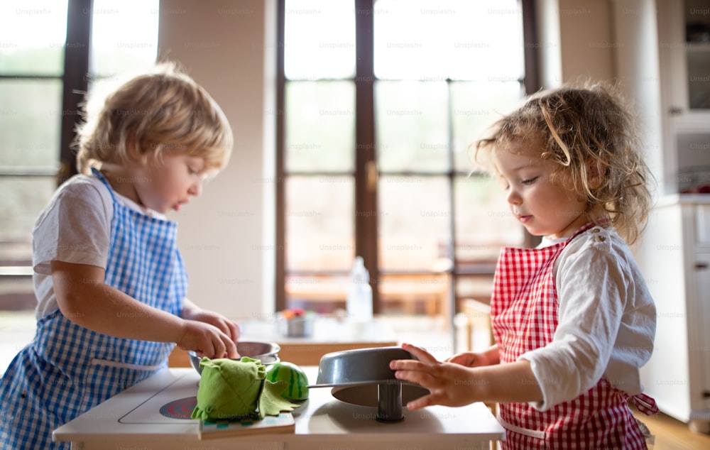 Bambino e ragazza felici con grembiule che giocano all'interno con la cucina giocattolo a casa.