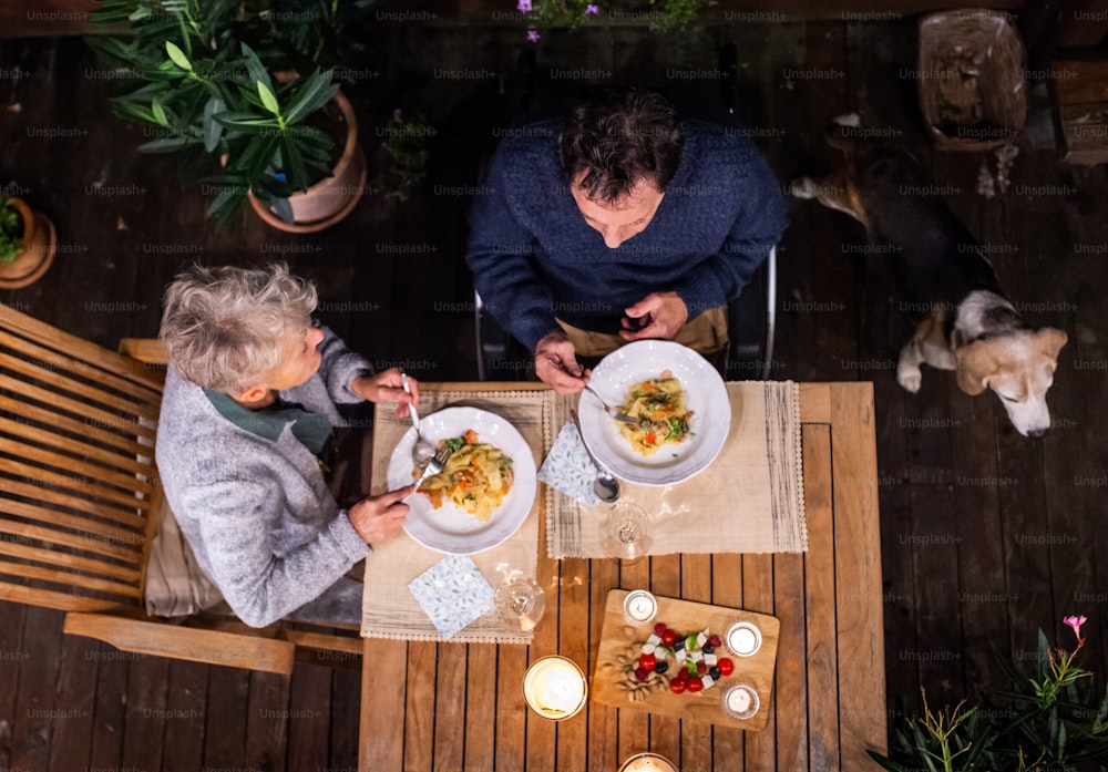Vista superior do casal idoso em cadeira de rodas jantando à noite no terraço, relaxando.