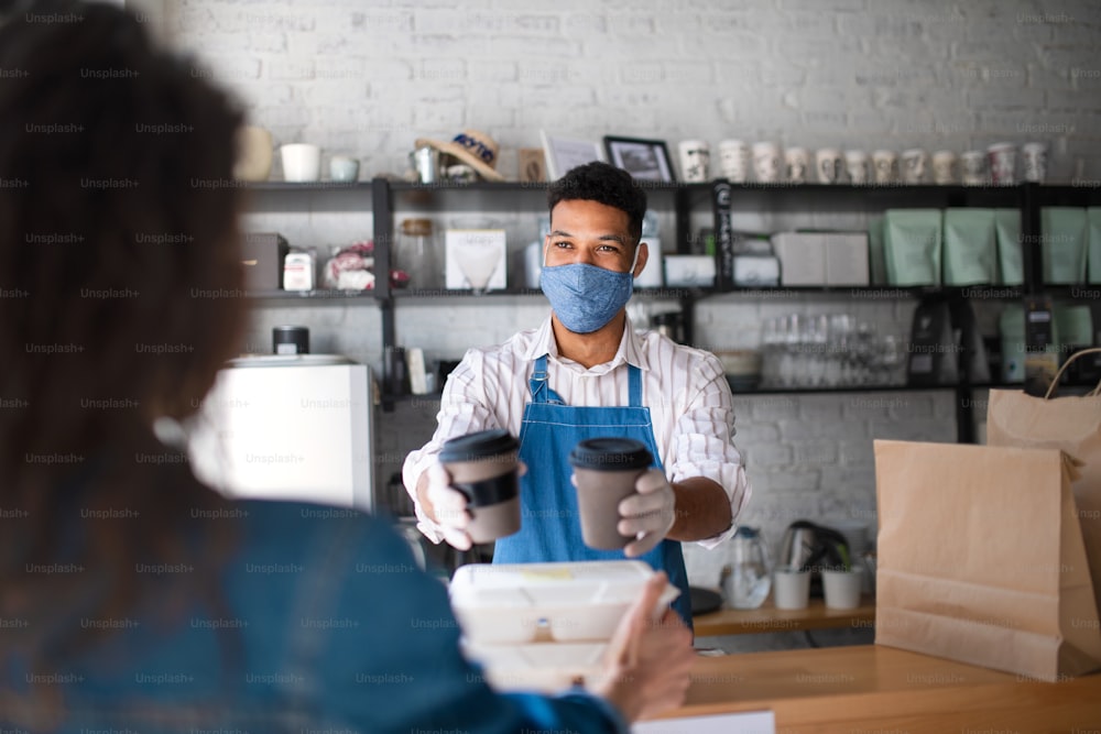 Un camarero que da comida para llevar y café envasados al cliente en una cafetería, concepto de coronavirus.