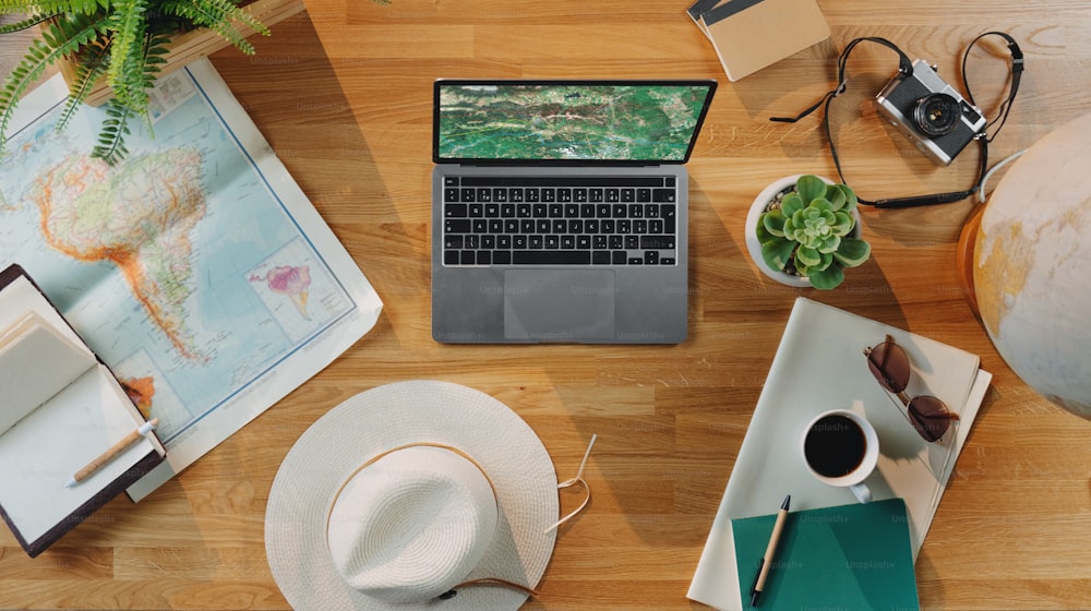 Flat lay top view desktop travel concept with laptop, maps and other travel essentials, wooden background.
