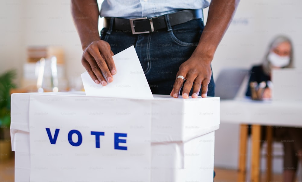 알아볼 수 없는 아프리카계 미국인 남성이 투표함, 미국 선거 및 코로나바이러스 개념에 투표를 하고 있습니다.