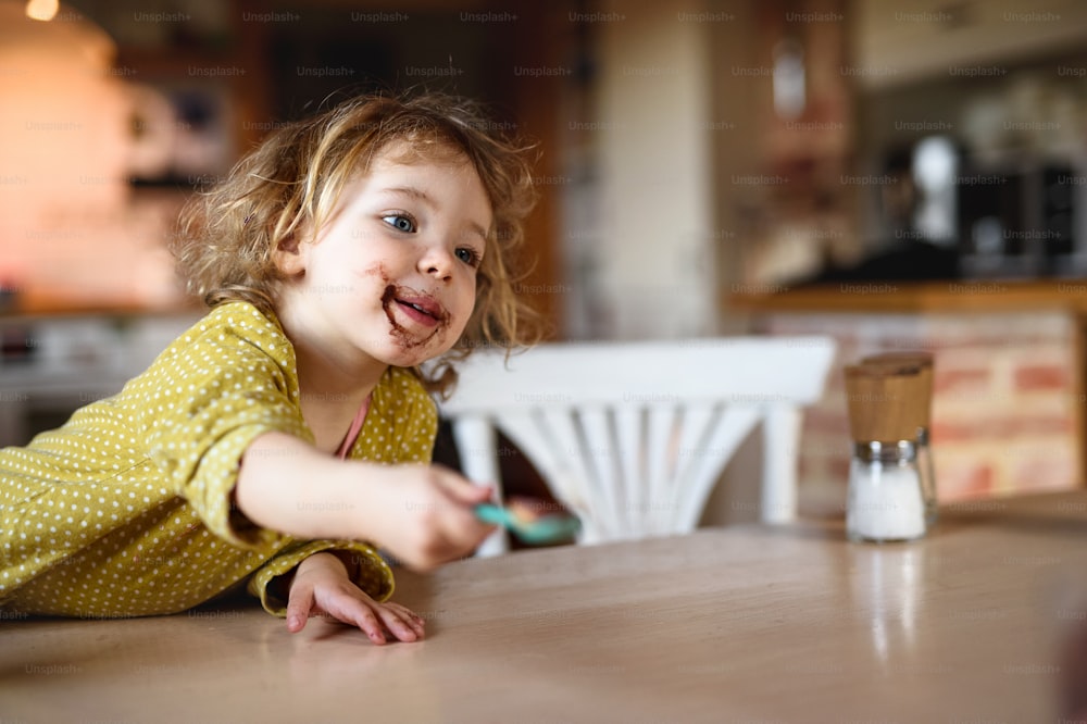 自宅の台所で口が汚い幸せな小さな女の子がプリンを食べています。