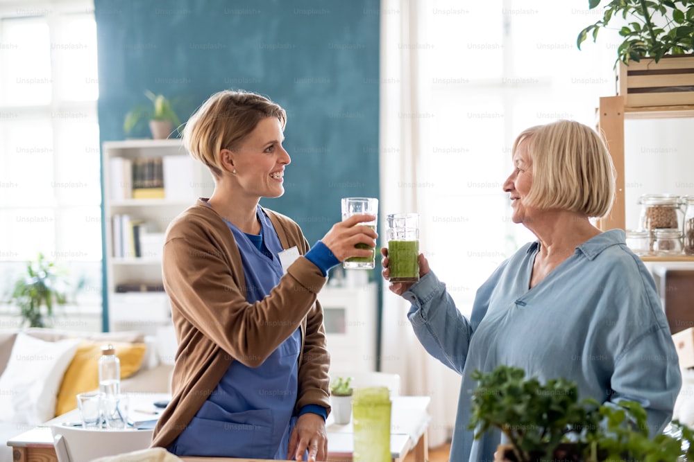 Senior woman with caregiver or healthcare worker indoors, drinking healthy smoothie drink.