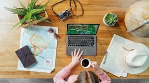 Top view of unrecognizable young woman with laptop and maps planning vacation trip holiday, desktop travel concept.