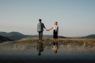 A portrait of young couple standing in nature in countryside, holding hands but looking away from each other.