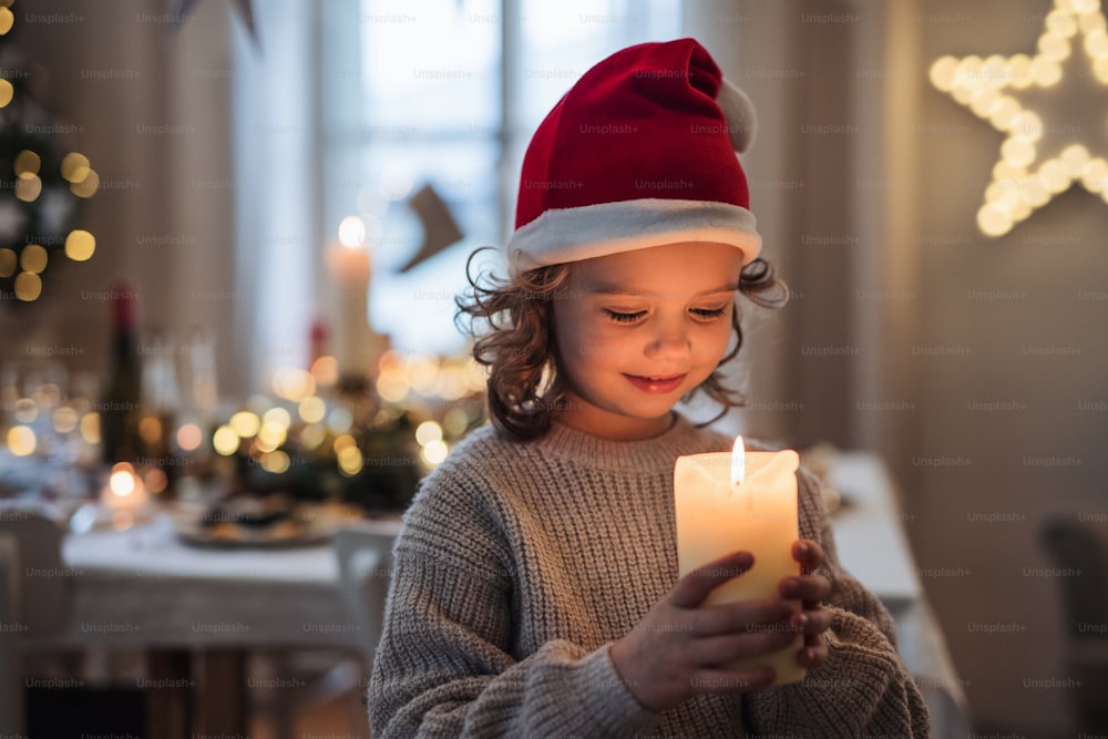 크리스마스에 실내에 서서 촛불을 들고 서 있는 행복한 작은 소녀의 전면 모습.