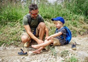 Père mûr avec son petit fils faisant de la randonnée en plein air dans la nature estivale, mettant du plâtre sur le genou.