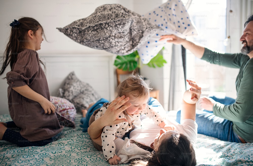 Retrato da família feliz com duas filhas pequenas se divertindo na cama em casa.