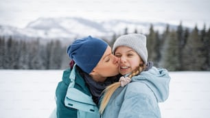 Portrait d’une mère embrassant sa petite fille à l’extérieur dans la nature hivernale, montagnes des Tatras, Slovaquie.