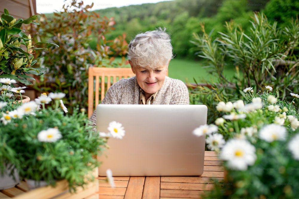 Portrait of senior woman with laptop sitting on terrace in summer, resting.