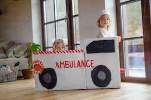 Two small children with doctor uniforms and toy ambulance car indoors at home, playing.