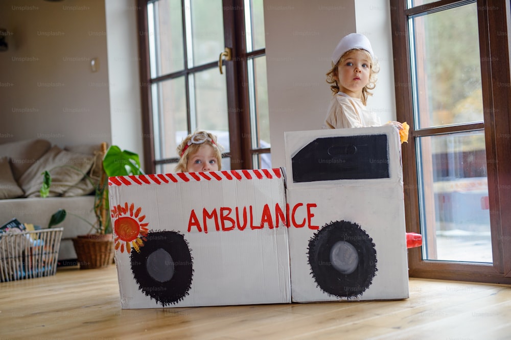 Due bambini piccoli con uniformi da medico e auto ambulanza giocattolo all'interno di casa, giocando.