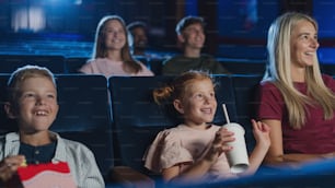 A mother with happy small children in the cinema, watching film.