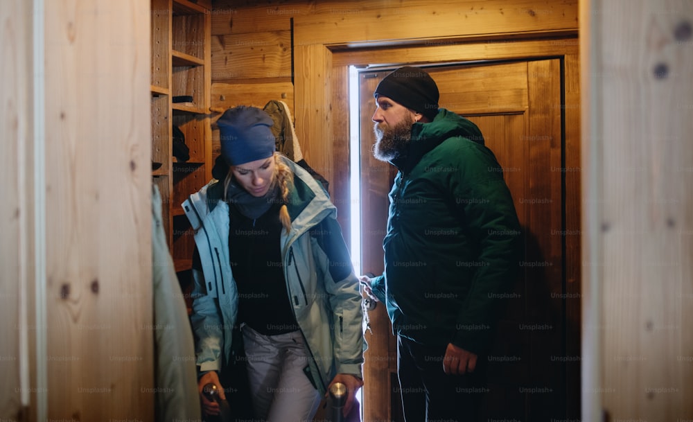 Portrait of mature couple entering wooden hut, holiday in winter nature concept.