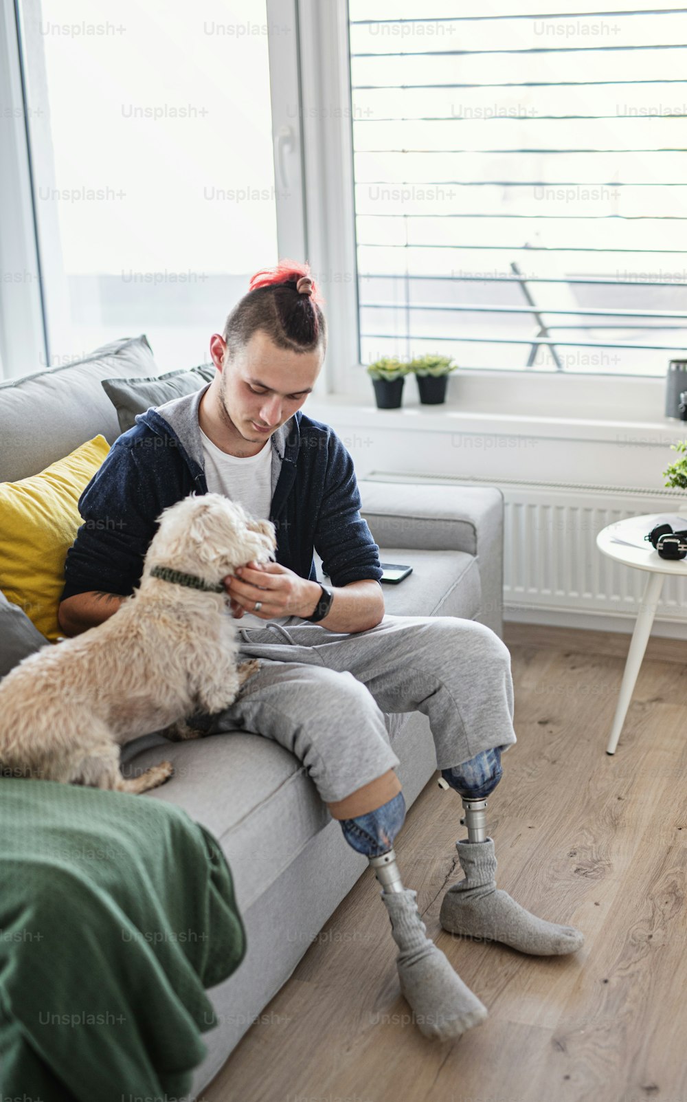 A portrait of disabled young man playing with dog indoors at home, leg prosthetic concept.