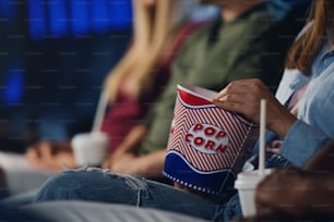 Midsection of unrecognizable young woman with popcorn in the cinema, watching film.