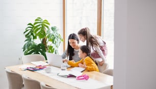Mother with school girls indoors at home, distance learning and home office coccept.