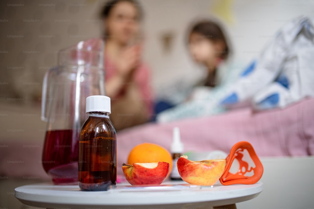 Jug with tea, medication syrup, fruit and inhaler on bedside table, illness and sickness concept.