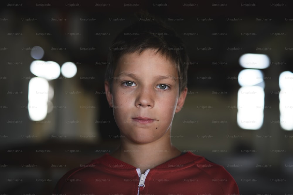 Trauriger und enttäuschter Teenager-Junge, der drinnen in einem verlassenen Gebäude auf einem Stuhl steht und in die Kamera schaut.
