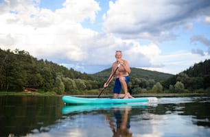 Happy senior man paddleboarding on lake in summer. Copy space.