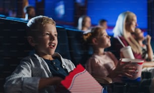 Un niño pequeño con familia sentado y viendo películas en el cine, comiendo palomitas de maíz