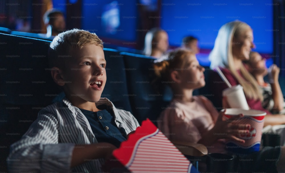 A small boy with family sitting and watching film in the cinema, eating popcorn