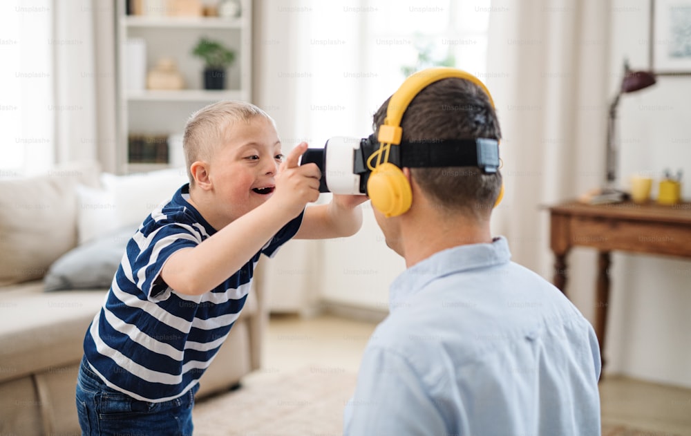 A father with happy down syndrome son indoors at home, using vr goggles.