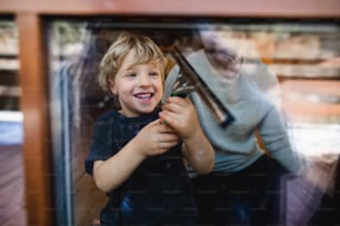 Um menino feliz com pai irreconhecível limpando janelas em casa, conceito de tarefas diárias.