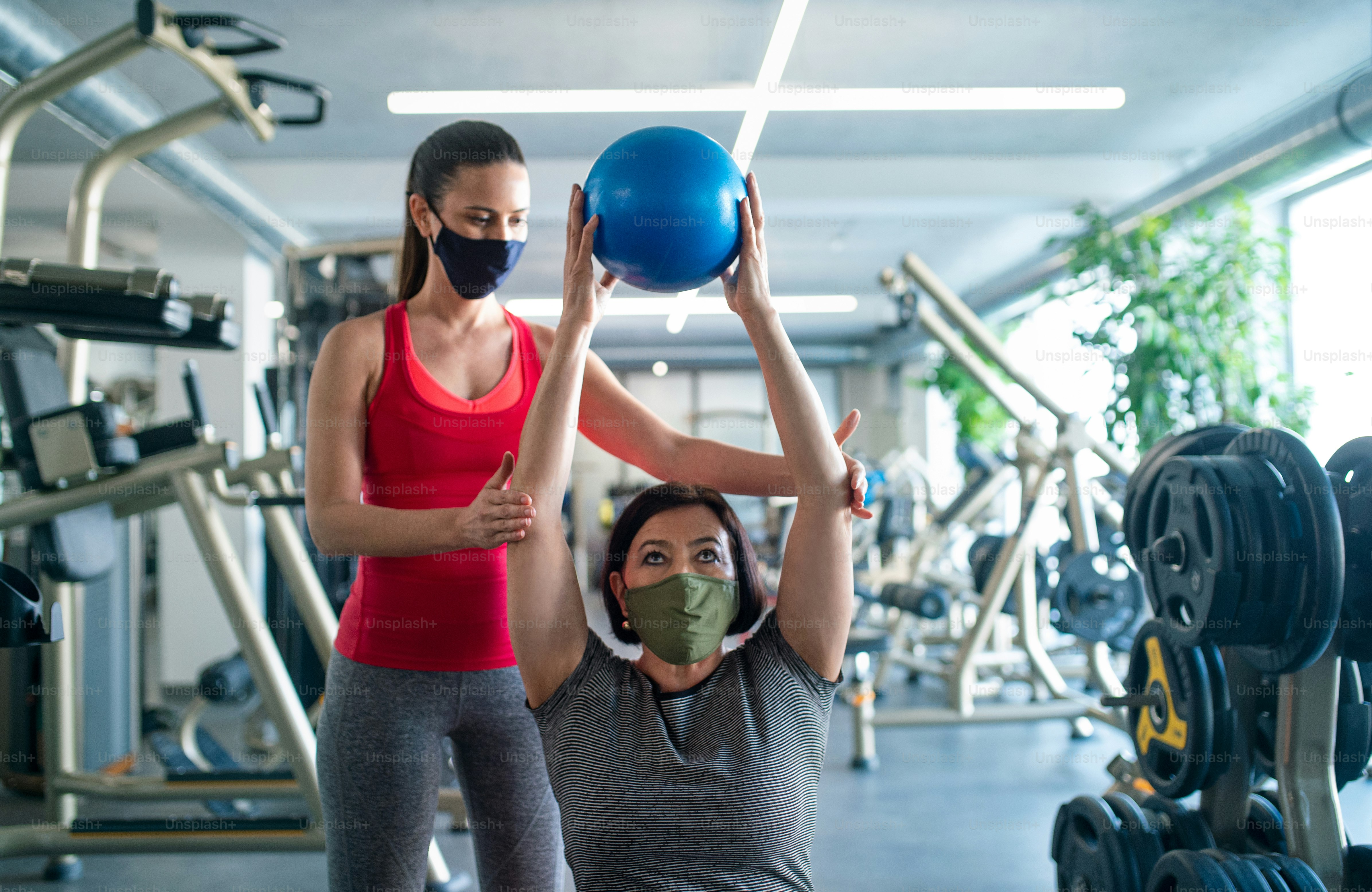 Active senior woman with personal trainer doing exercise in gym, coronavirus concept