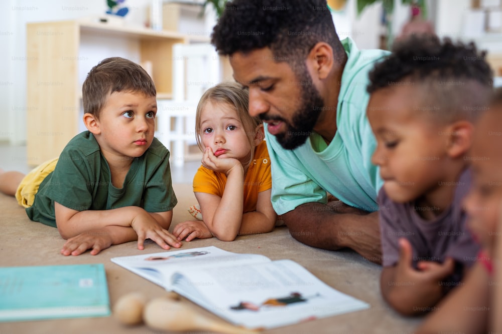 小さな保育園の子どもたちと、教室の床で男性教師が本を読んでいるグループ。