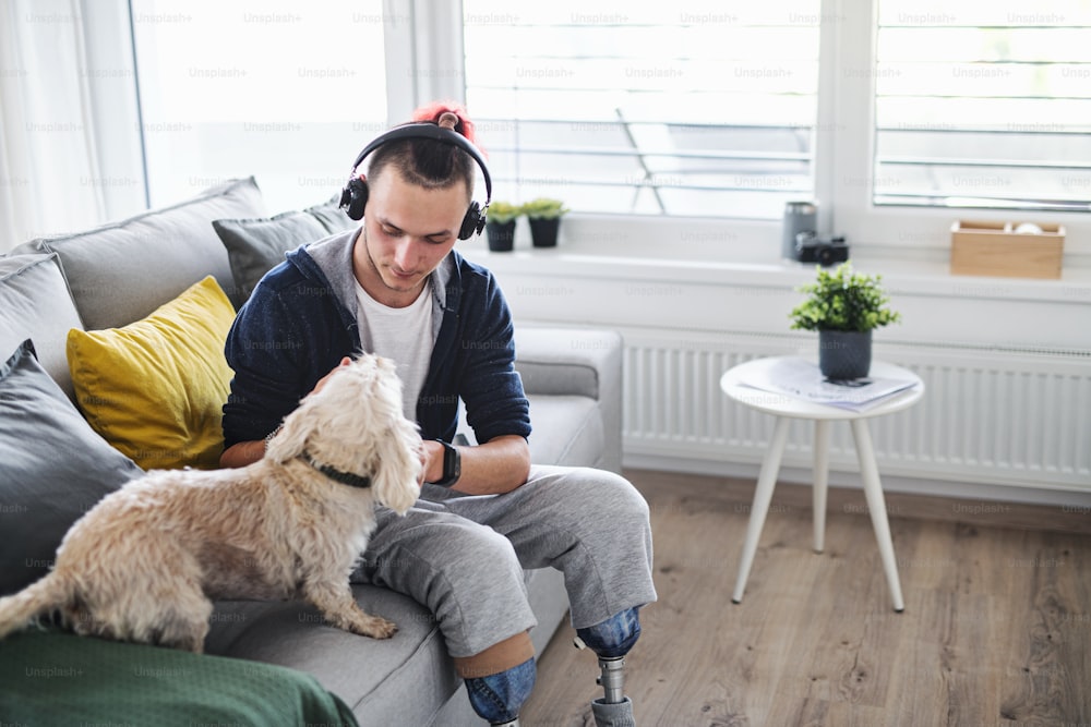 自宅の室内で犬と遊んでいる障害のある若い男性の肖像画、義足のコンセプト。