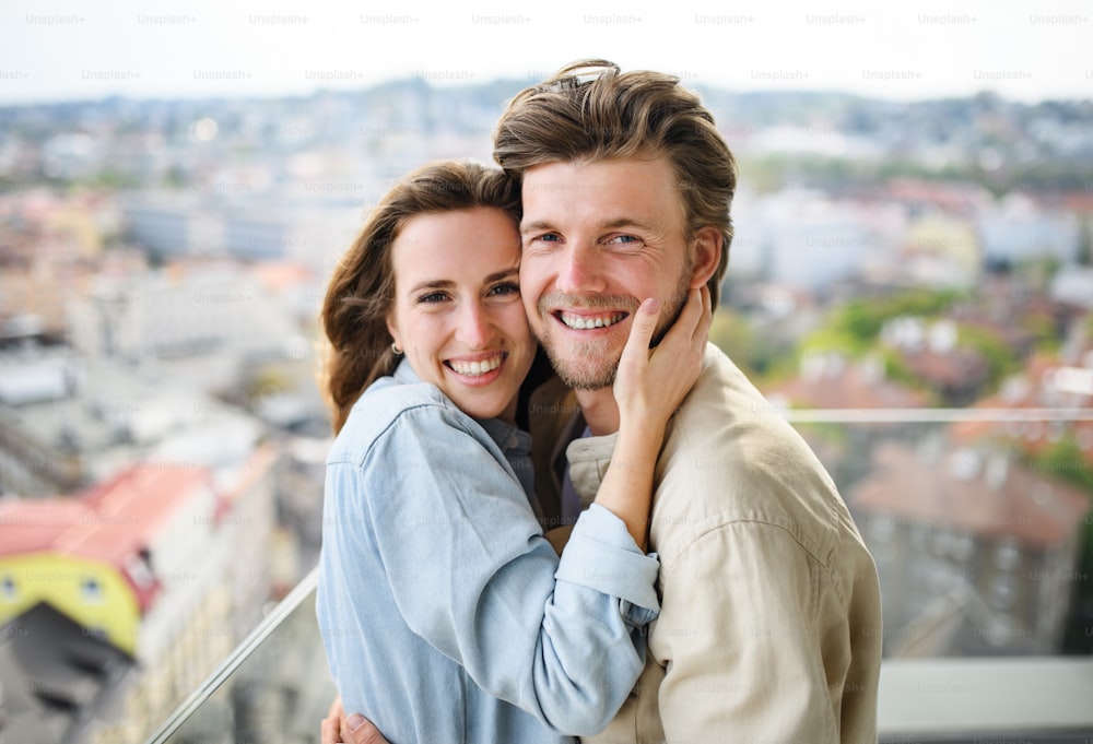 Una giovane coppia felice innamorata che guarda la telecamera all'aperto sul balcone di casa, abbracciandosi.