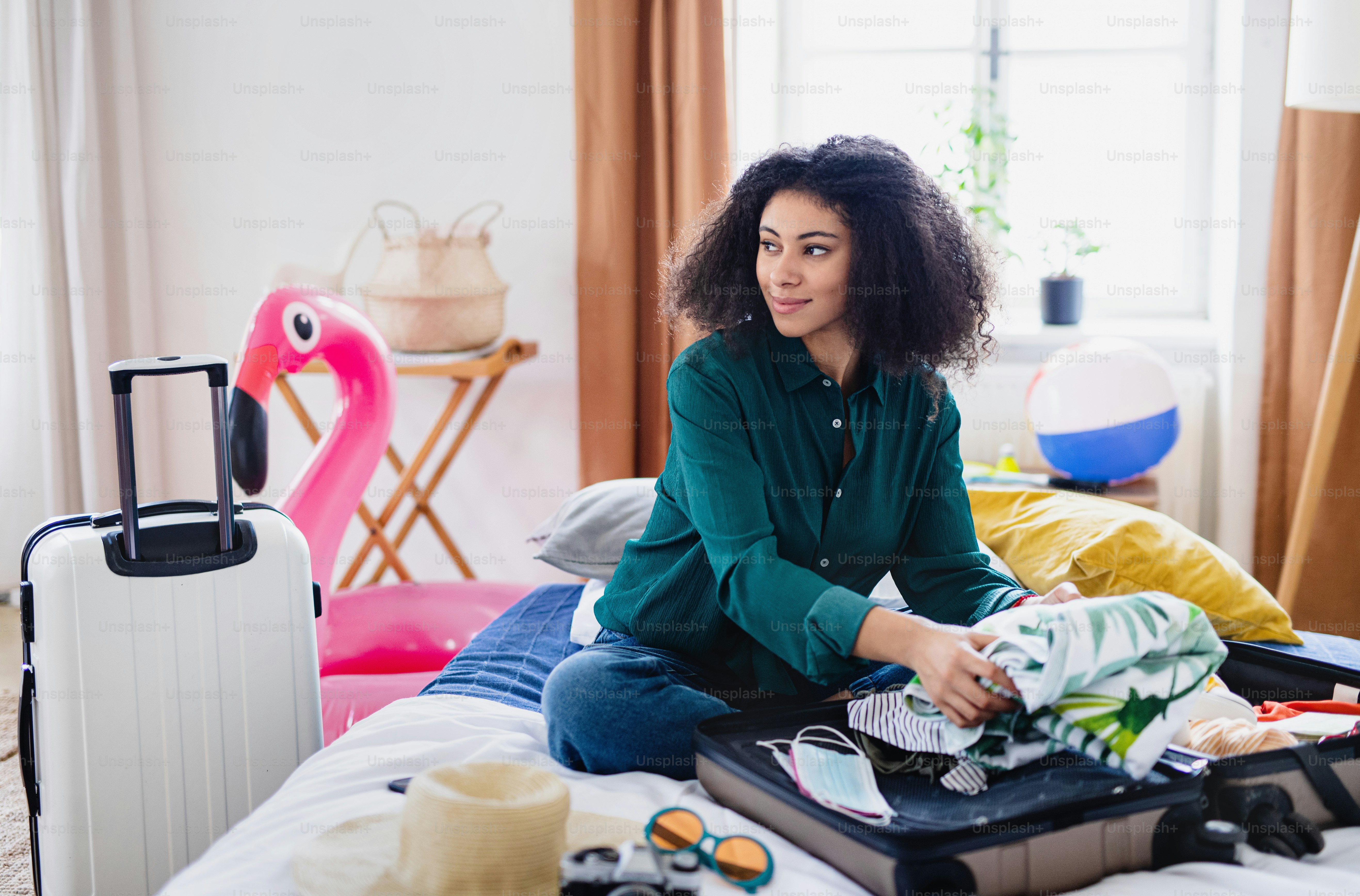 自宅での休日のためのスーツケースの梱包、コロナウイルスのコンセプトを持つ幸せな若い女性。