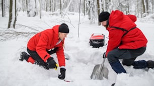 Mountain rescue service on operation outdoors in winter in forest, digging snow with shovels. Avalanche concept.
