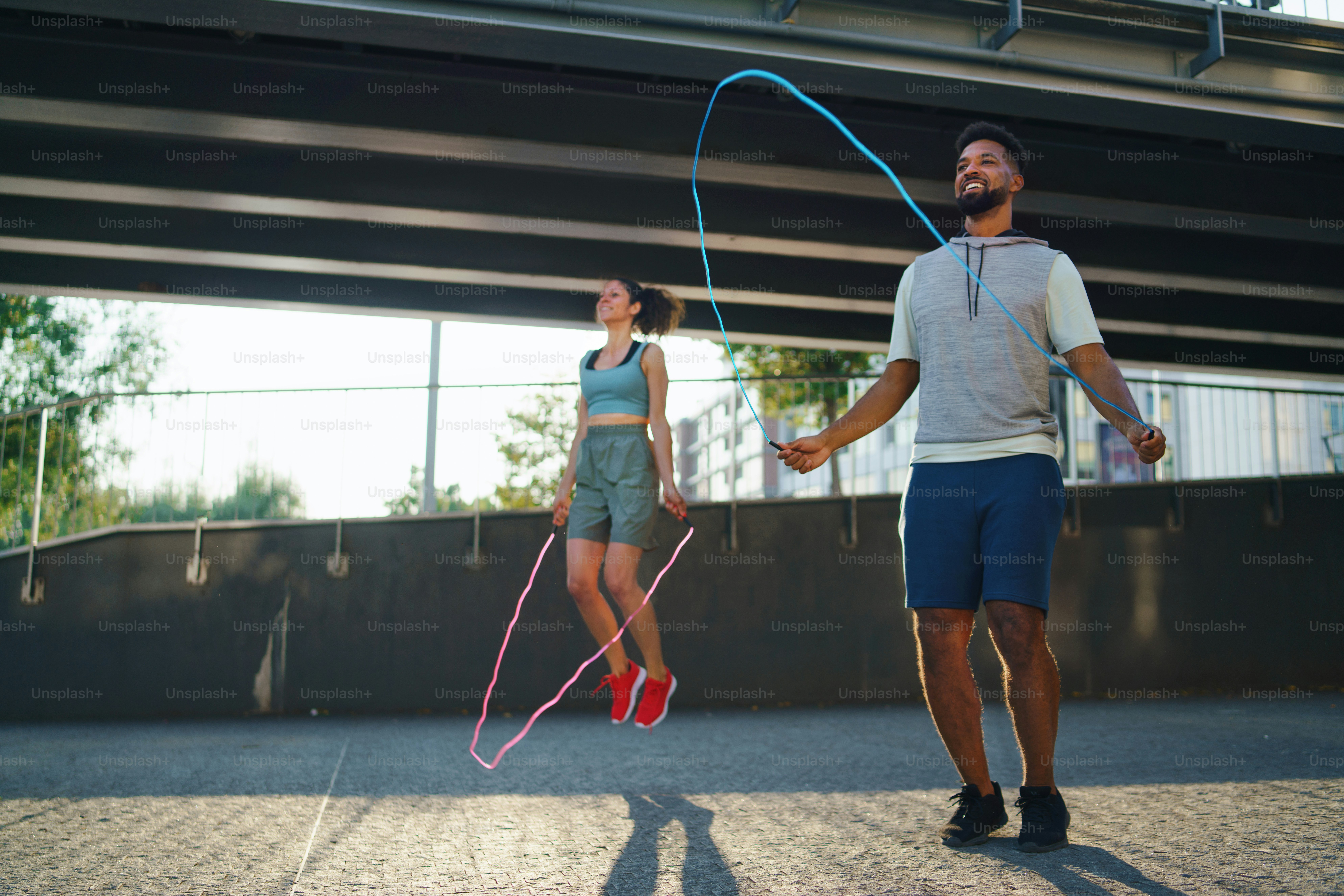 Happy man and woman couple friends doing workout exercise outdoors in city, skipping.