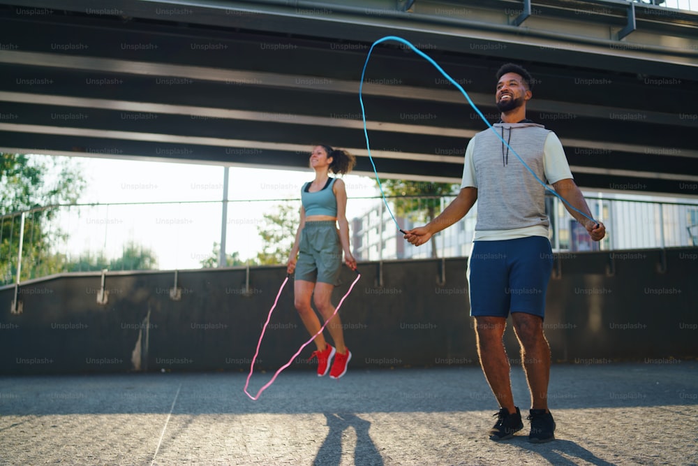 Happy man and woman couple friends doing workout exercise outdoors in city, skipping.