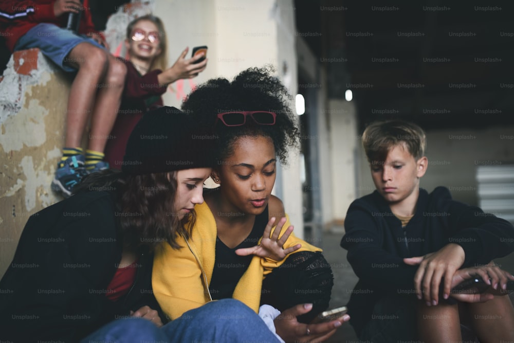 Vista frontal de un grupo de adolescentes sentados en el interior de un edificio abandonado, usando teléfonos inteligentes.