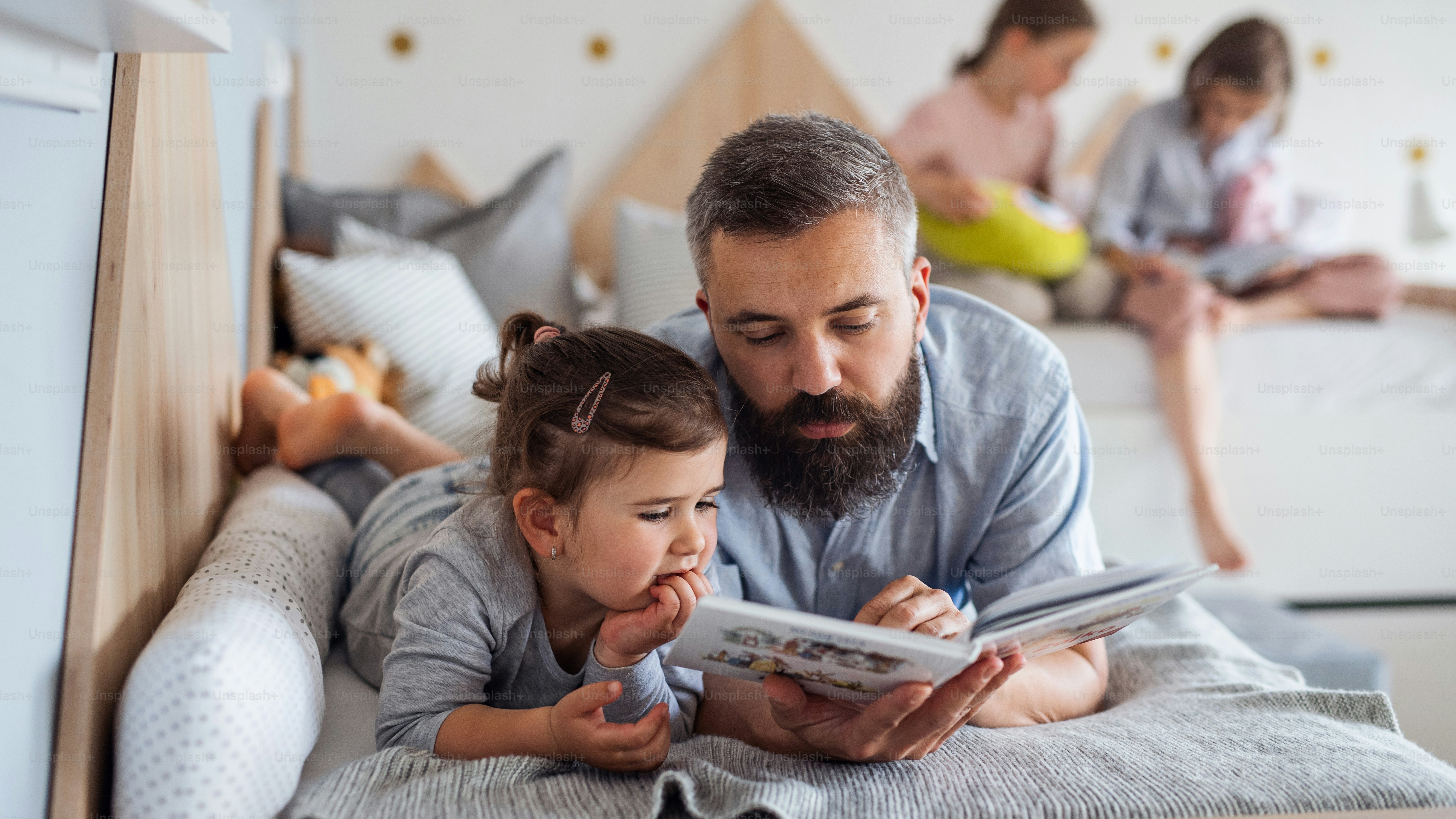 A father with three daughters indoors at home, reading a book