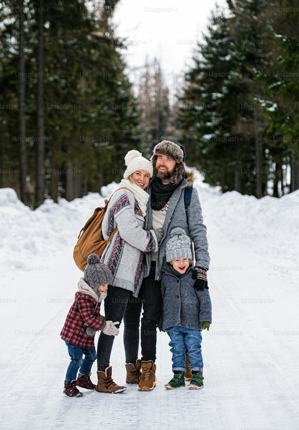 Front view portrait of father and mother with two small children in winter nature, standing in the snow.