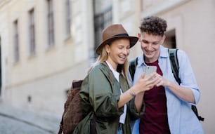 Viajeros de pareja joven que caminan con smarthone en la ciudad de vacaciones, haciendo turismo.