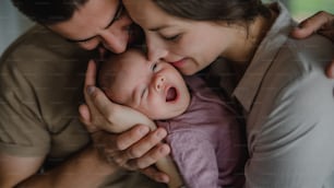 Close up of happy young parents holding and kissing their newborn baby indoors at home
