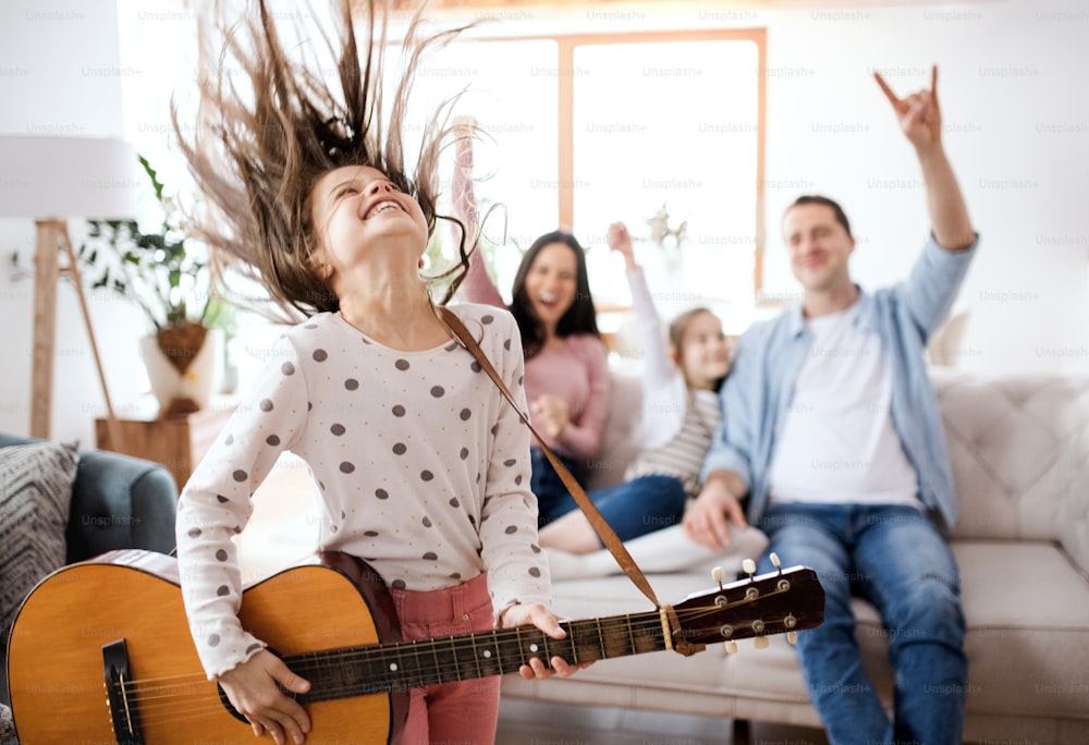 Portrait of small girl with family indoors at home, having fun with guitar.