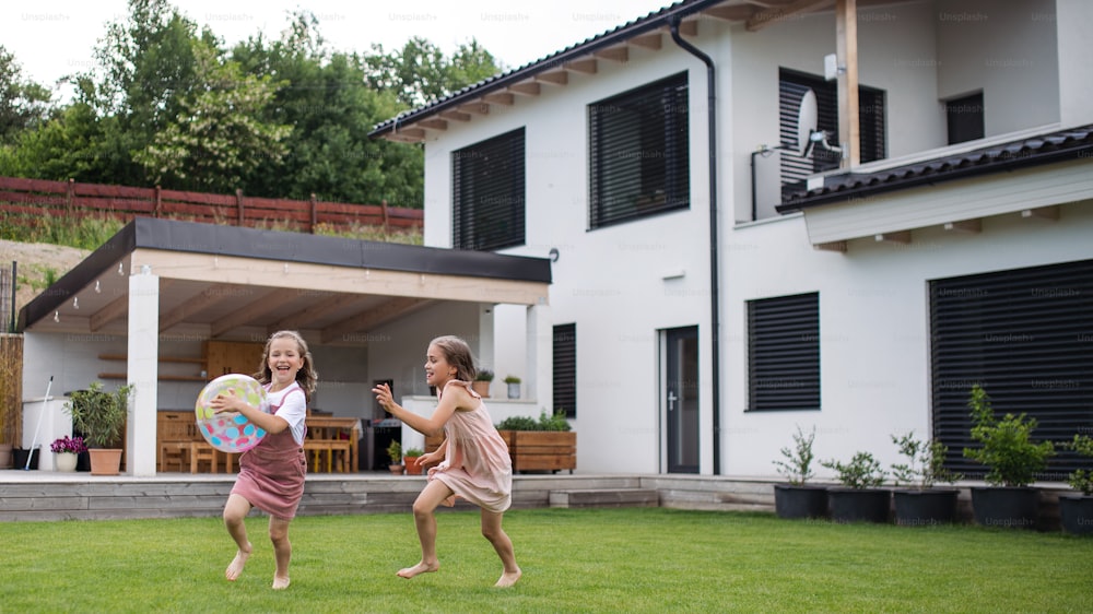 두 명의 행복한 작은 소녀 자매가 뒤뜰에서 야외에서 공을 가지고 놀고 있습니다.
