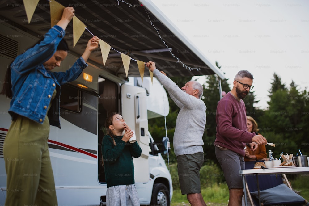 Felice famiglia multigenerazionale che prepara la festa in auto all'aperto in campeggio, viaggio di vacanza in roulotte.