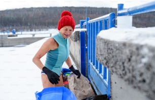 An active senior woman in swimsuit outdoors in winter, cold therapy concept.